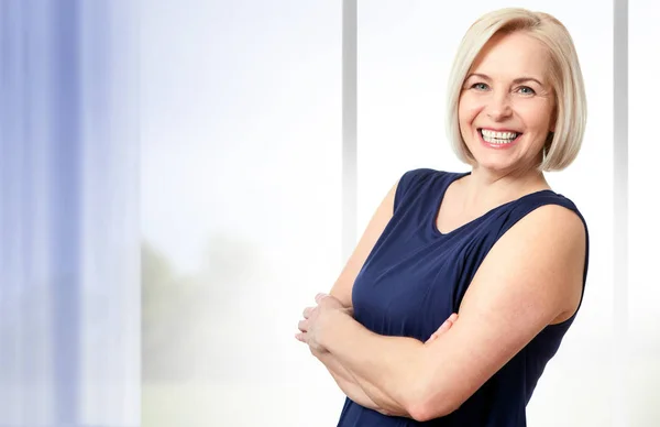 Attractive middle aged woman with a beautiful smile near the window. — Stock Photo, Image