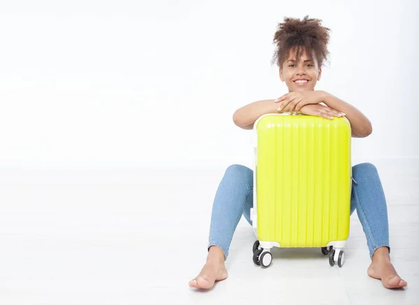 A girl with a yellow suitcase is sitting near the white wall. The concept of summer holidays — Stock Photo, Image