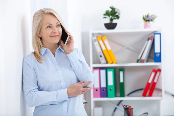 Улыбающийся бизнесмен средних лет разговаривает по телефону в офисе . — стоковое фото