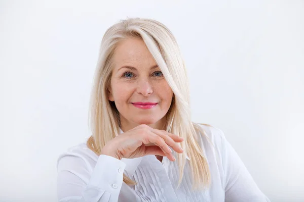 Schöne blonde Frau mittleren Alters mit einem strahlenden Lächeln, die im Büro sitzt und in die Kamera schaut — Stockfoto