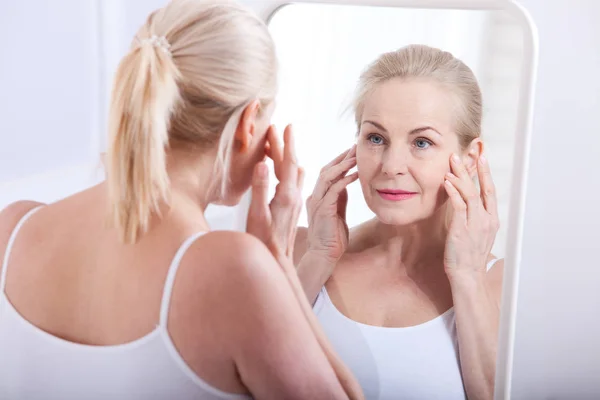 Mujer de cuarenta años mirando las arrugas en el espejo. Cirugía plástica e inyecciones de colágeno. Maquillaje. Cara de macro. Enfoque selectivo — Foto de Stock