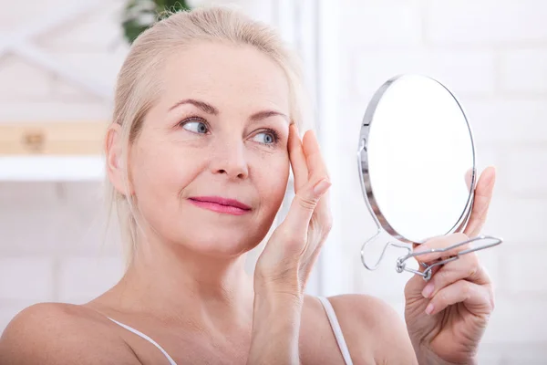 Forty years old woman looking at wrinkles in mirror. Plastic surgery and collagen injections. Makeup. Macro face. Selective focus — Stock Photo, Image