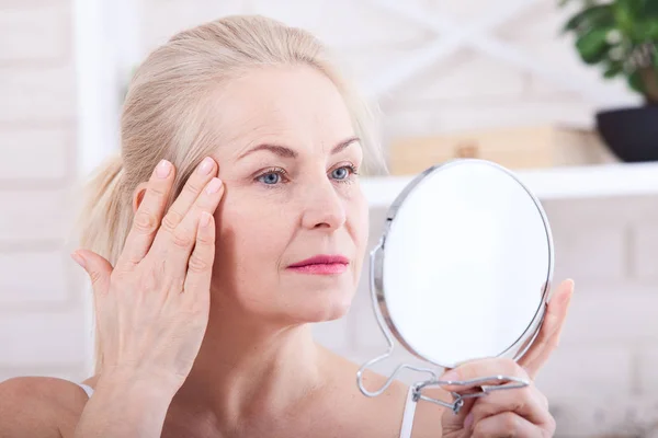 Forty years old woman looking at wrinkles in mirror. Plastic surgery and collagen injections. Makeup. Macro face. Selective focus — Stock Photo, Image