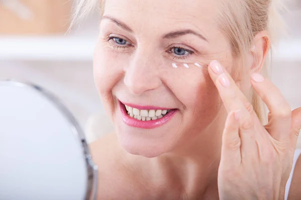 Mujer de cuarenta años mirando las arrugas en el espejo. Cirugía plástica e inyecciones de colágeno. Maquillaje. Cara de macro. Enfoque selectivo — Foto de Stock