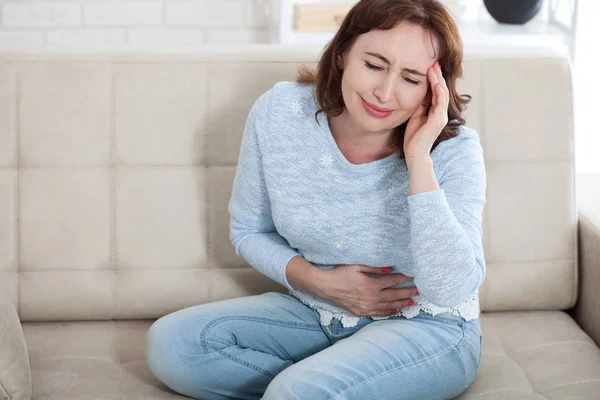 Donna di mezza età che soffre di dolore addominale mentre seduto su — Foto Stock