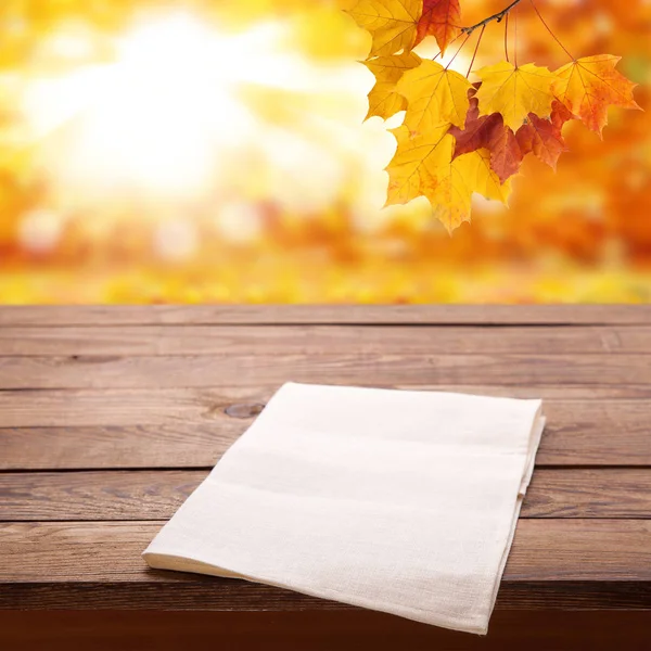 Tabulka prázdná dřevěná paluba s ubrus nad bokeh podzim listy pozadí. Kuchyňské zázemí, produkt montáž displeje. Vysmívat se . — Stock fotografie