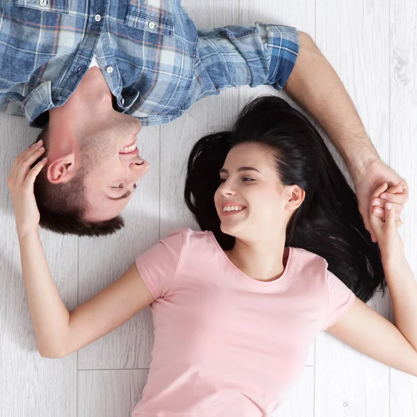 Ein glückliches junges Paar, auf dem Boden liegend, blickt sich an und träumt von Möbeln für eine neue Wohnung. Attrappe — Stockfoto