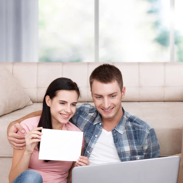Kaunis nuori pari kannettavan tietokoneen avulla kommunikoi Skypen kautta. Nainen hymyilee ja näyttää tyhjää paperia . — kuvapankkivalokuva