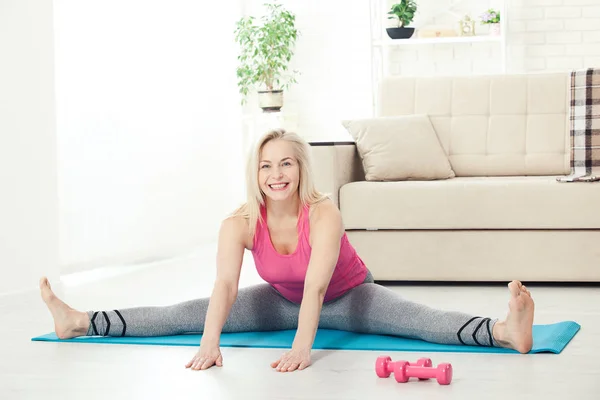 Lycklig kvinna i hennes 50s stretching för träning hemma. Glädje av l — Stockfoto