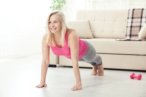 Glückliche Frau in ihren Fünfzigern, die sich zu Hause für Sport dehnt. Freude über l — Stockfoto