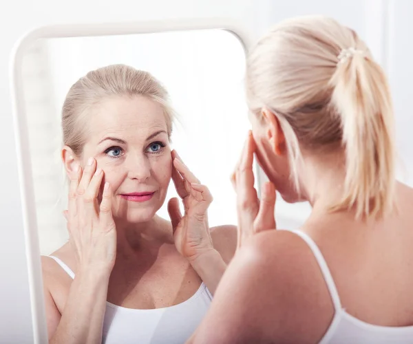 Mujer de mediana edad mirando las arrugas en el espejo. Cirugía plástica e inyecciones de colágeno. Maquillaje. Cara de macro. Enfoque selectivo — Foto de Stock