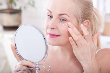 Forty years old woman looking at wrinkles in mirror. Plastic surgery and collagen injections. Makeup. Macro face. Selective focus clipart