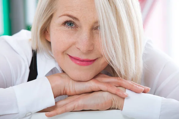 Szép szőke középkorú nő egy ragyogó mosoly ül az office néz a kamerába — Stock Fotó