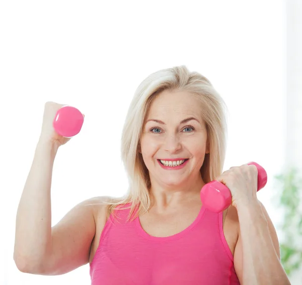 Happy middle aged woman lifting dumbbells at home in the living room Royalty Free Stock Images