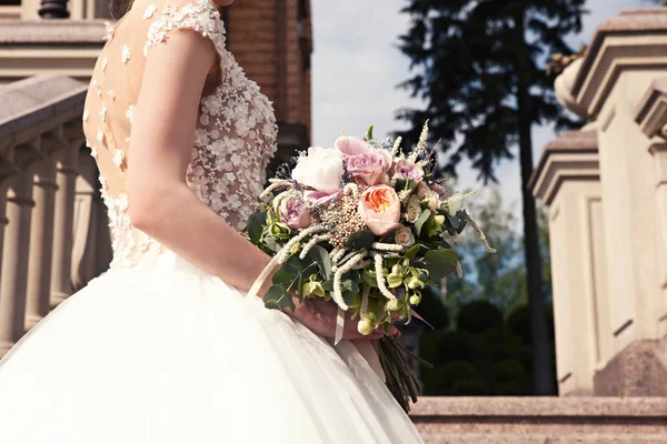 Ung brud i en vit klänning med en vacker brudbukett på en marmortrappa i ett gammalt slott. Bruden håller en brudbukett, vackra brudklänning, bröllop Detaljer. Bröllop ceremoni koncept. — Stockfoto