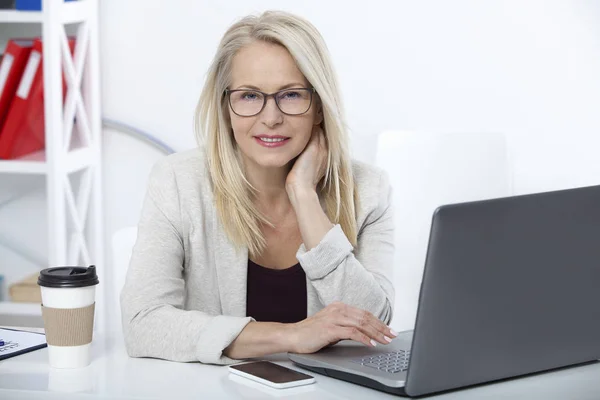 Hennes jobb är hennes liv. Affärskvinna med glasögon som arbetar på kontor med dokument. Vackra mellersta år kvinna som tittar på kamera med leende medan placering i office. — Stockfoto