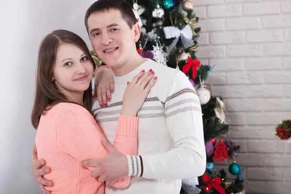 Jovem casal apaixonado em pé junto à lareira e árvore de Natal bem decorada, desfrutando da magia de Natal . — Fotografia de Stock