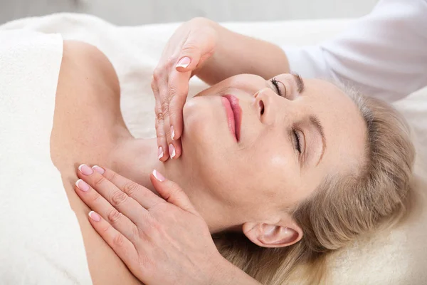 Retrato de mujer hermosa en ambiente spa. mujer de mediana edad haciendo masaje facial en un salón de spa — Foto de Stock