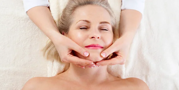 Retrato de mulher bonita em ambiente de spa. mulher de meia idade fazendo massagem facial em um salão de spa — Fotografia de Stock