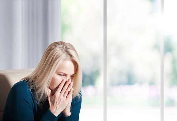 Frau, die unter Stress oder Kopfschmerzen leidet, Grimassen vor Schmerzen. Traurige depressive Frau zu Hause, die auf der Couch sitzt, nach unten schaut und ihre Stirn berührt. — Stockfoto