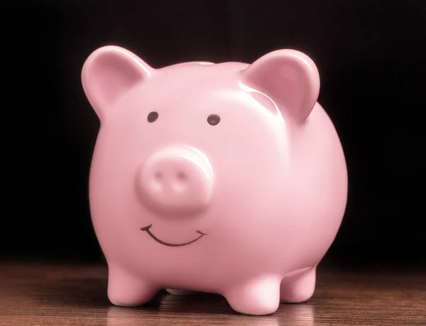 木桌上的粉红色小猪银行 黑色背景 — 图库照片