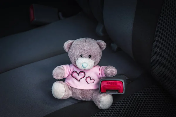 Small teddy bear seating in a car without safety belt. Child safety in a car concept.