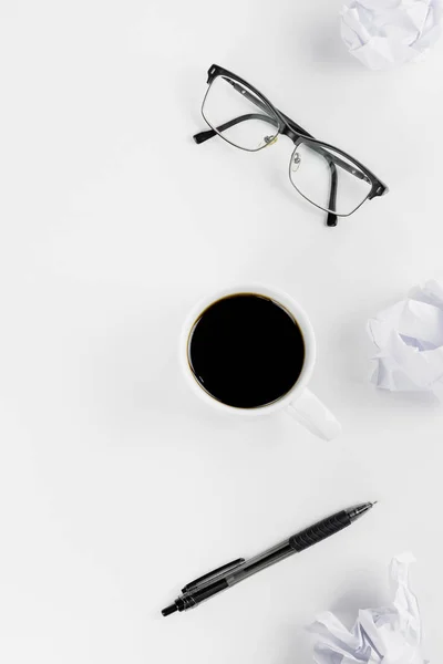 Tabletop of a writer/ content creator. Vertical flat lay with crumpled paper, coffee cup, glasses and pen on a white table. Creative writing process with copy space.