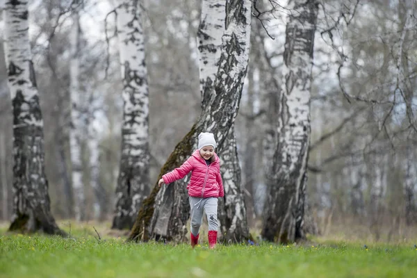 Um pequeno bebê encaracolado em uma jaqueta rosa e botas divertido corre na floresta de primavera. As primeiras flores. Símbolo suave da primavera. Cuidar de uma nova vida. Conceito de feriado do dia da Terra. Dia Mundial do Ambiente — Fotografia de Stock