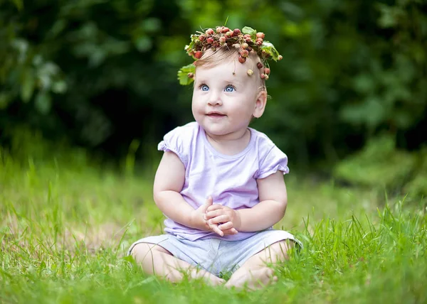Милая улыбающаяся девочка с венком из клубничных цветов в зеленом лесу в солнечный летний день — стоковое фото