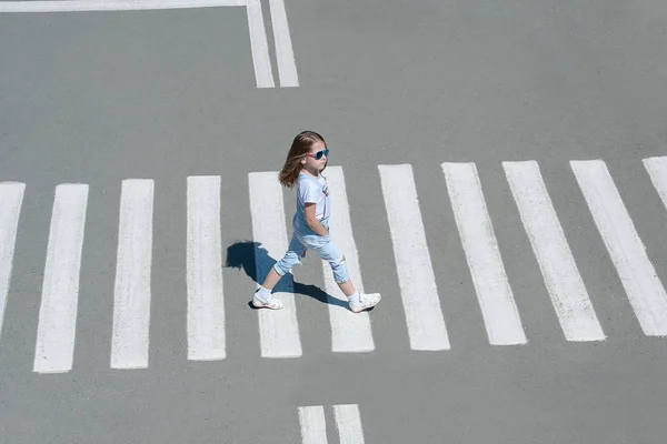 No verão na rua no pedestre que cruza a menina de criança com a roupa de moda cruza a estrada. Da vista de cima. Sombra na travessia de zebra — Fotografia de Stock
