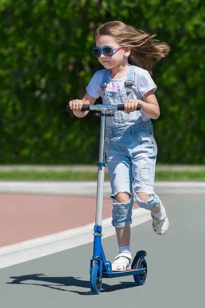 Kind fährt Roller. Kind auf buntem Kickboard. aktiver Outdoor-Spaß für Kinder. Sommersport für Vorschulkinder. kleines glückliches Mädchen im Frühlingspark. das Konzept eines gesunden Lebensstils — Stockfoto