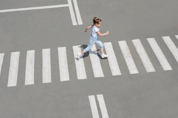 Yaz aylarında sokakta yaya geçidinde moda giysileri çocuk kız yolun karşısına geçin. En tepeden bak. Zebra geçişinde gölge — Stok fotoğraf