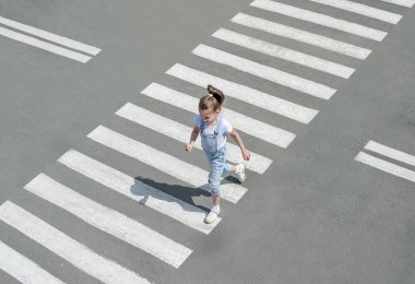 Yaz aylarında sokakta yaya geçidinde moda giysileri çocuk kız yolun karşısına geçin. En tepeden bak. Zebra geçişinde gölge