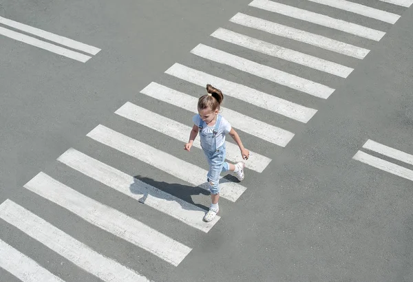 In the summer on the street at the pedestrian crossing kid girl in fashion clothes cross the road. From top view. Shadow at zebra crossing