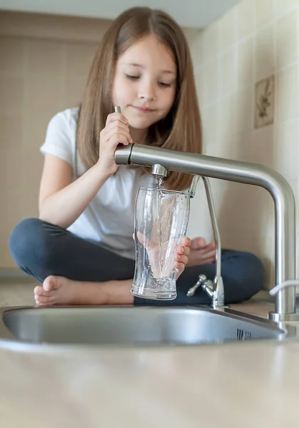 Pouring water into a glass. A little caucasian girl pours water from a tap into a transparent glass. The concept of saving and problems with water, lack of water in various regions of the world