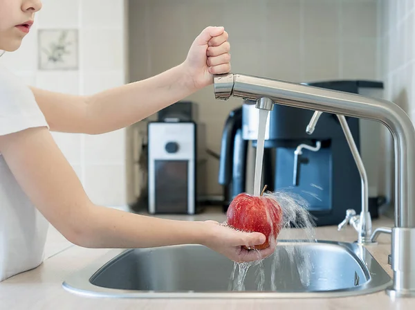 A cute little girl washes a red yellow apple in a sink. Child is washing the fruit in kitchen. Little child learns the rules of hygiene. Child uses the tap himself. Healthy lifestyle hygiene concept