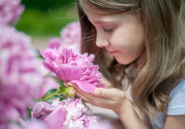 Uzun saçlı, çiçek kokan sevimli küçük kız. Çiçek açan pembe şakayık (Paeonia, şakayık) çiçek. Açık havada. Doğanın tadını çıkarın. Bahar parkında sağlıklı gülümseyen çocuk. Alerji ücretsiz kavramı. Özgürlük