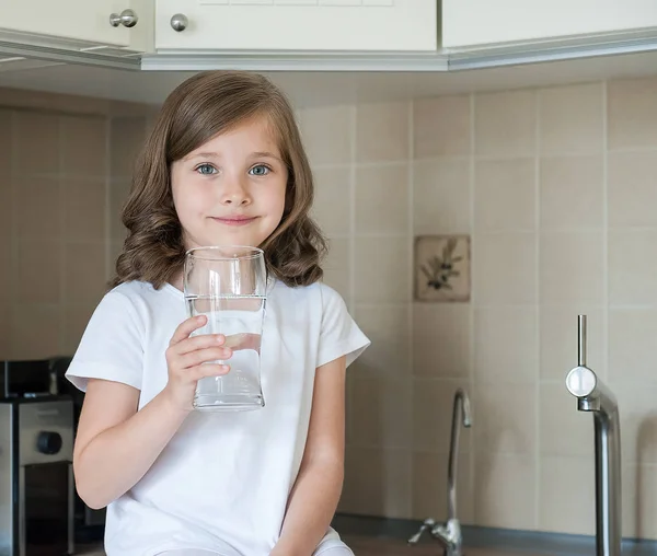 Elinde bir bardak musluk temiz su tutan küçük beyaz bir kız bebek portresi. Mutfak musluğu. Sevimli çocuk filtre musluğundan tatlı su döküyor. Kapalı. Sağlıklı yaşam kavramı