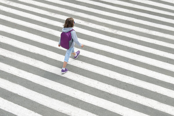 Schoolgirl crossing road on way to school. Zebra traffic walk way in the city. Concept pedestrians passing a crosswalk. Top view