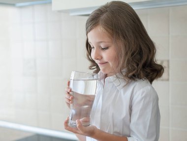 Küçük çocuk evde temiz su içiyor, yakın. Uzun saçlı Kafkas sevimli kız elinde bir su camı tutuyor. Kendi sağlığına bakıyorum. Sağlıklı yaşam konsepti, iyi alışkanlık