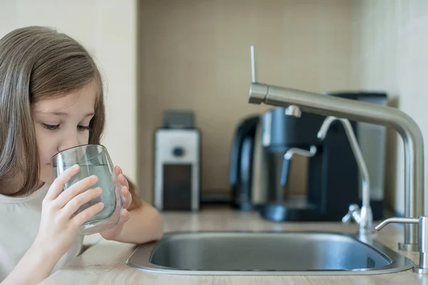 Küçük çocuk camdan taze ve saf musluk suyu içiyor. Mutfak musluğundan bardağa su dökülüyor. Sıfır israf ve plastik bilinçli minimalizm yaşam tarzı konsepti yok. Çevre ve ekoloji
