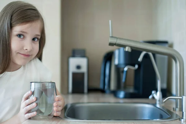 Elinde temiz bir bardak su tutan gülümseyen küçük kız. Musluk suyu tüketimi plastik şişelerde su tasarrufuna ve çevrenin korunmasına katkıda bulunur. Dünya Su İzleme Günü