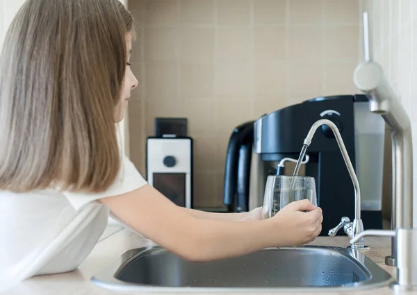 Child pouring fresh reverse osmosis purified water in kitchen at home. Drinking tap water. Consumption of tap water contributes to the saving of water in plastic bottles. Protection of the environment