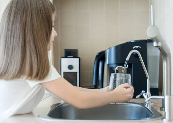 Evdeki mutfakta taze ters osmoz döken çocuk arıtılmış su. Musluk suyu içmek. Musluk suyu tüketimi plastik şişelerde su tasarrufuna katkıda bulunur. Çevreyi koruma