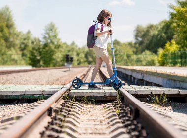 Gündüz vakti demiryolu rayları boyunca ahşaptan yapılmış rayları geçmek. Scooter 'ı taşıyan ve yolu geçen kız öğrenci. Yaya geçidinden geçen bir yaya. Yol kullanıcıları için güvenlik kavramı