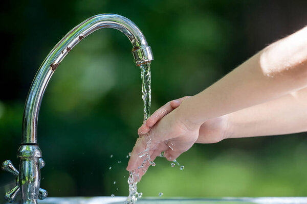 Маленький ребенок моет руки чистой водой в парке. Гигиена кистей коронавируса. Концепция гигиены, чистоты и здравоохранения. Поток воды из крана. На улице. Естественный зеленый фон