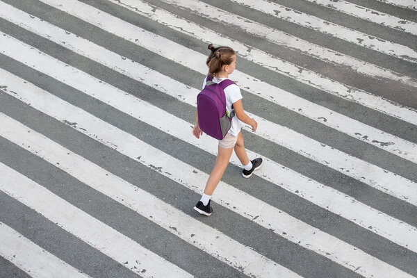 Schoolgirl crossing road on way to school. Zebra traffic walk way in the city. Concept pedestrians passing a crosswalk.  Stylish young teen girl walking with backpack. Active child. Top view