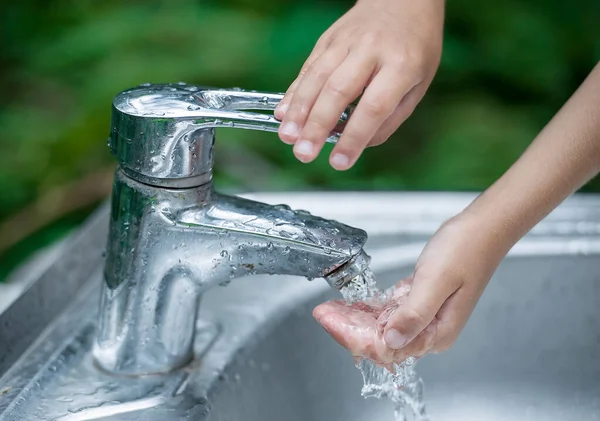 Baby try to turn off water faucet but water still leak. A child's hand turning off the tap. Save water. World Water Monitoring Day. Environment and health care concept. Natural green background