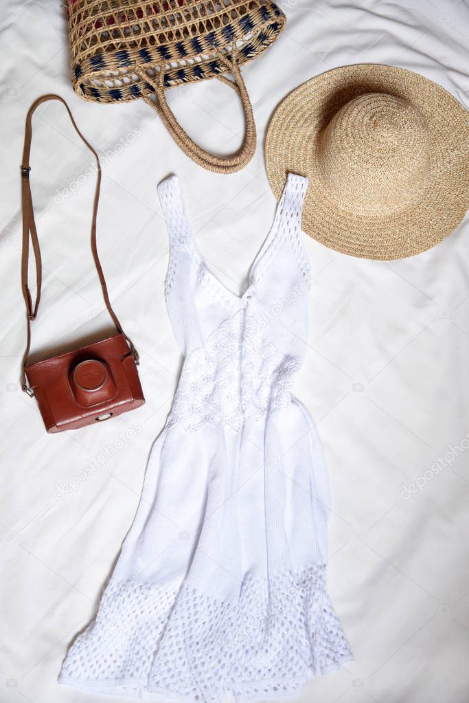 Woman fashion travel. Vintage retro camera,knitted dress,straw hat and bag on a white bed. Top view. Flat lay.