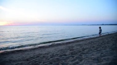 Ekose gömlek ve şort deniz kıyısında güzel pembe günbatımı gökyüzü çalışan çocuk